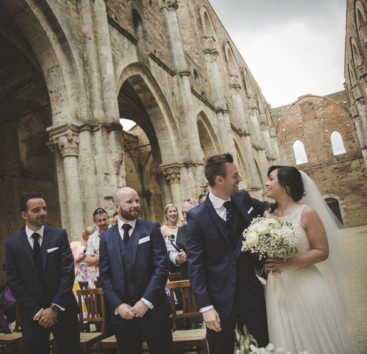 Outdoor Ceremony Bride Lace Sleeveless Bridal Gown Loose Curls Veil Bouquet Cream Roses Gypsophila Groom Navy Blue Suit Polka Dot Tie Groomsmen Guests Atmospheric Abbey Tuscany Wedding http://www.angelicabraccini.com/