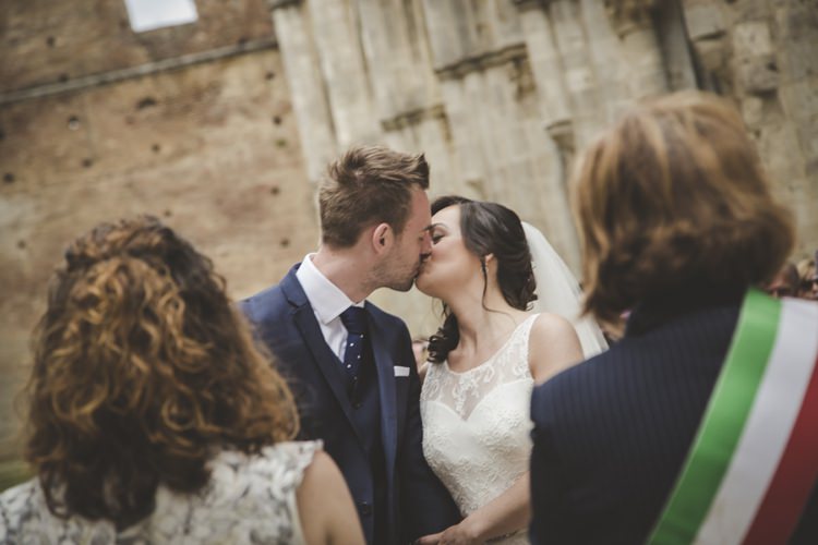 Outdoor Ceremony Bride Lace Sleeveless Bridal Gown Loose Curls Veil Groom Navy Blue Suit Polka Dot Tie White Pocket Square Kiss Guests Atmospheric Abbey Tuscany Wedding http://www.angelicabraccini.com/