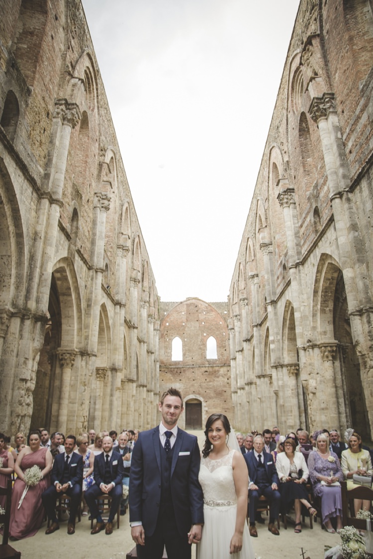 Outdoor Ceremony Bride Lace Sleeveless Bridal Gown Beaded Belt Loose Curls Veil Groom Navy Blue Suit Polka Dot Tie White Pocket Square Bridesmaids Groomsmen Guests Gypsophila Flowers Atmospheric Abbey Tuscany Wedding http://www.angelicabraccini.com/