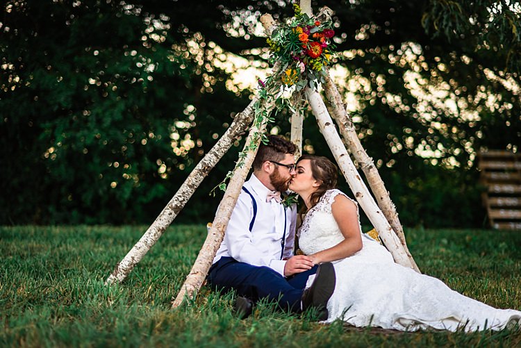Bride Lace Bridal Gown With Buttons Groom Navy Pants Suspenders Cream Bow Tie Teepee Multicoloured Florals Pink Yellow Red Cushions Trees Grass Ethereal Boho Wedding Ideas http://perfectcapturephoto.com/