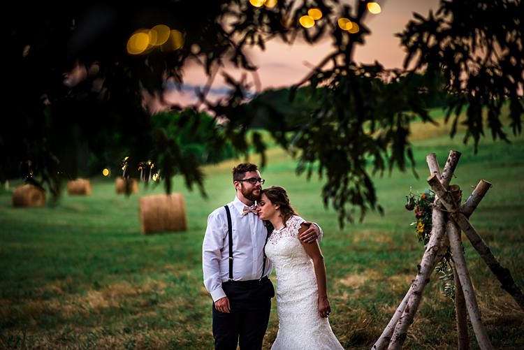 Bride Lace Bridal Gown With Buttons Groom Navy Pants Suspenders Cream Bow Tie Teepee Multicoloured Florals Grass Hay Bales Trees Sunset Ethereal Boho Wedding Ideas http://perfectcapturephoto.com/