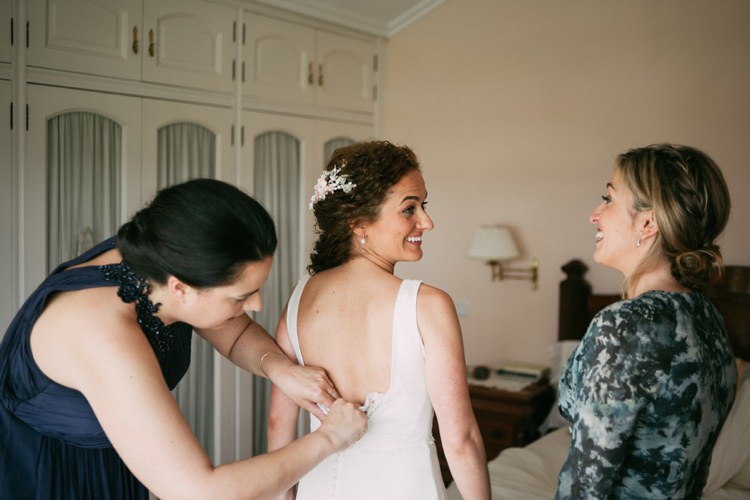 Bride Preparations Round Neck Low Back Crepe Tulle Bridal Gown Getting Dressed Floral Hair Piece Soft Makeup Smiles Romantic Bohemian Spain Wedding http://saralobla.com/