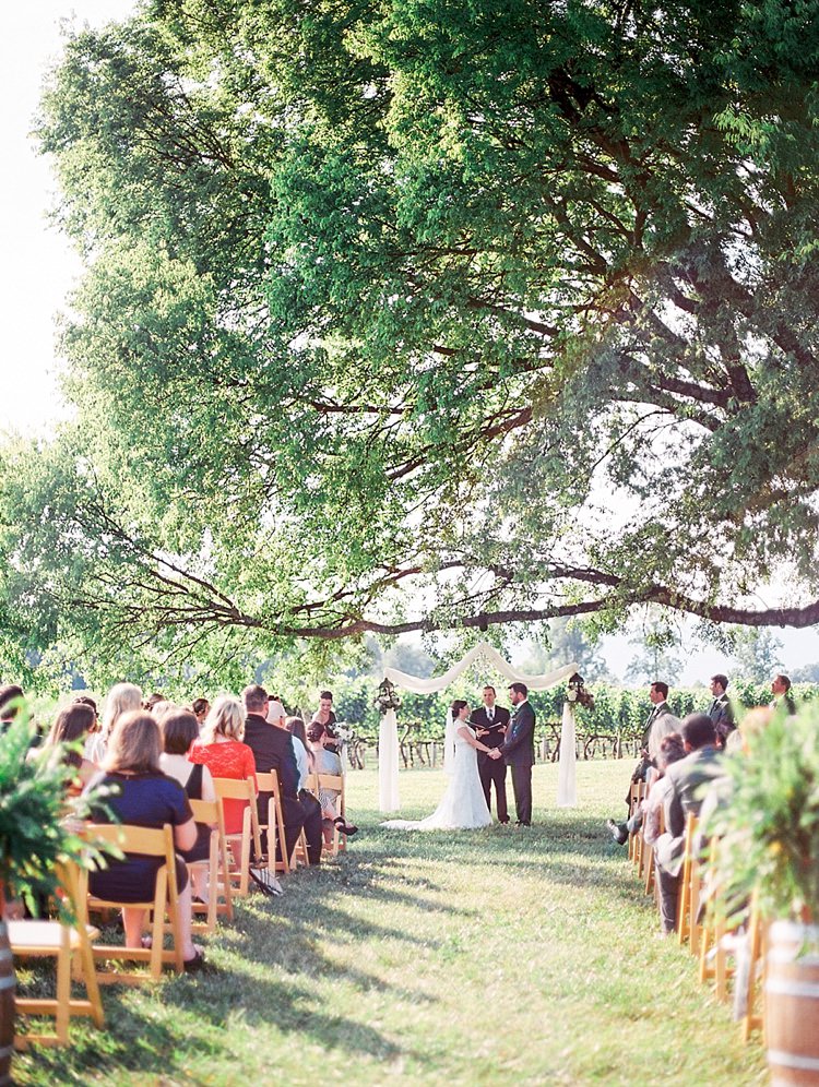 Outdoor Ceremony Bride Groom Celebrant Large Leafy Tree Guests Wooden Chairs Outdoor Spring Vineyard Wedding Tennessee http://www.juicebeatsphotography.com/