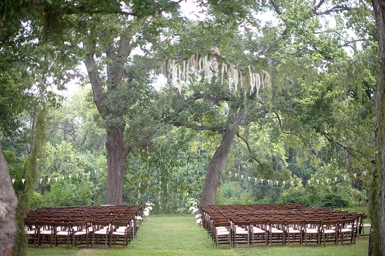 Outdoor Ceremony Hanging Bunting Dark Wooden Chairs Trees Grass Gold & Peach Riverside Garden Wedding http://kellyhornberger.com/