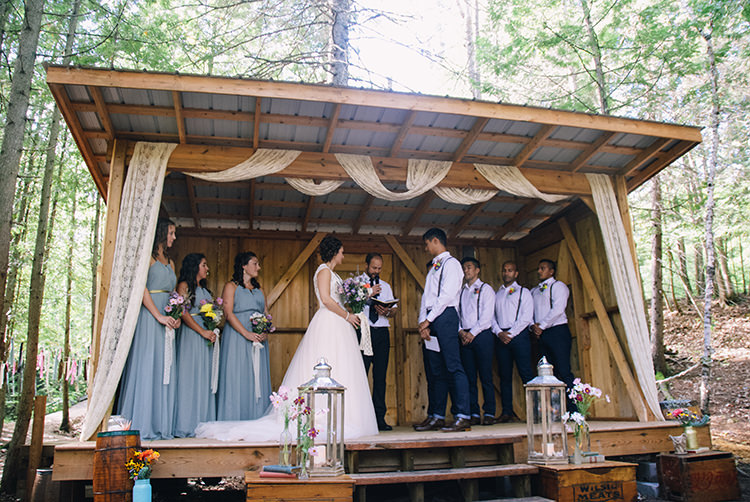 Outdoor Ceremony Bride Groom Bridesmaids Groomsmen Decorated Wooden Shelter Lace Silver Candle Lanterns Multicoloured Florals Vases Vintage Books Wooden Boxes Woodland Waterfall Mint Wedding Ontario http://www.laurenmccormickphotography.com/