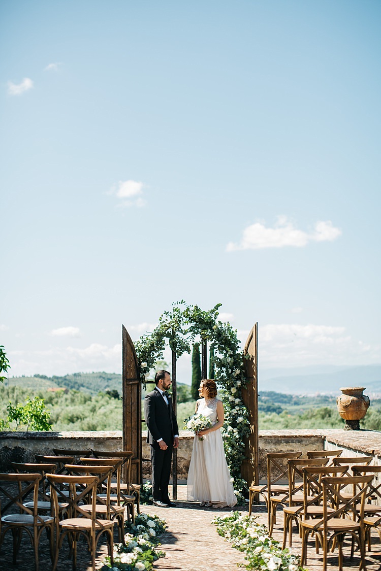 Outdoor Ceremony Bride High Neck Lace Tulle Bridal Gown Buttons Bouquet Groom Charcoal Pinstripe Suit Green Patterned Bowtie Wooden Archway White Roses Greenery Wooden Chairs Rustic Chic Greenery Wedding Ideas in Tuscany http://www.tastino0.it/