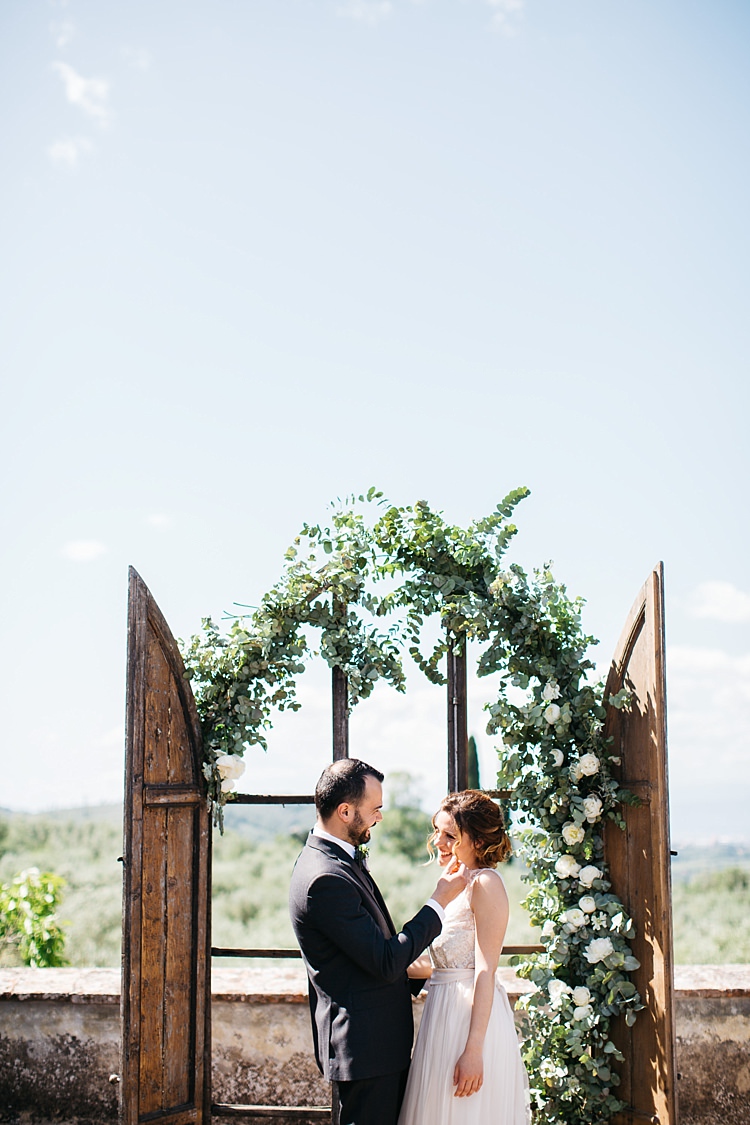 Outdoor Ceremony Bride High Neck Lace Tulle Bridal Gown Buttons Groom Charcoal Pinstripe Suit Green Patterned Bowtie Wooden Archway White Roses Greenery Rustic Chic Greenery Wedding Ideas in Tuscany http://www.tastino0.it/