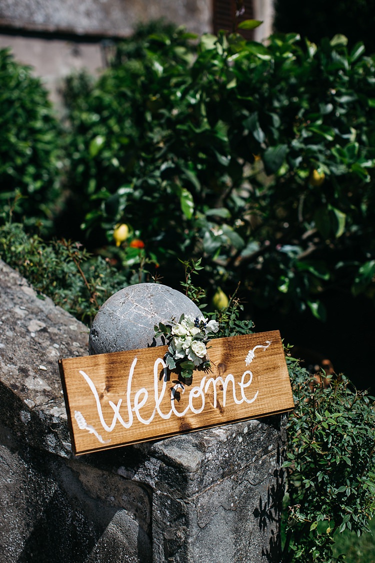 Outdoor Ceremony Wooden Welcome Sign White Handwriting Floral Decoration Stone Fence Trees Rustic Chic Greenery Wedding Ideas in Tuscany http://www.tastino0.it/