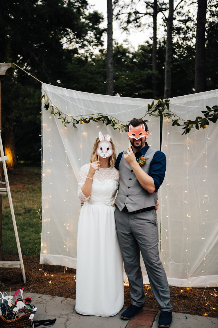 Reception DIY Photo Booth White Fabric Greenery Fairy Lights Masks Props Bride Handmade Lace Bridal Gown Groom Grey Vest Pants Navy Blue Shirt Adventure Inspired Woodland Wedding North Carolina http://www.amandasuttonphotography.com/