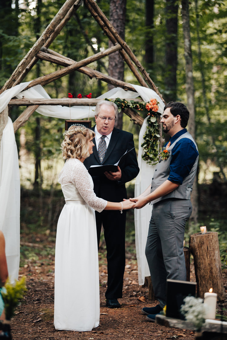 Outdoor Ceremony Bride Handmade Lace Bridal Gown Groom Grey Vest Pants Navy Blue Shirt Orange Tie Celebrant Decorated Wooden Arbour Fresh Florals Candles Adventure Inspired Woodland Wedding North Carolina http://www.amandasuttonphotography.com/