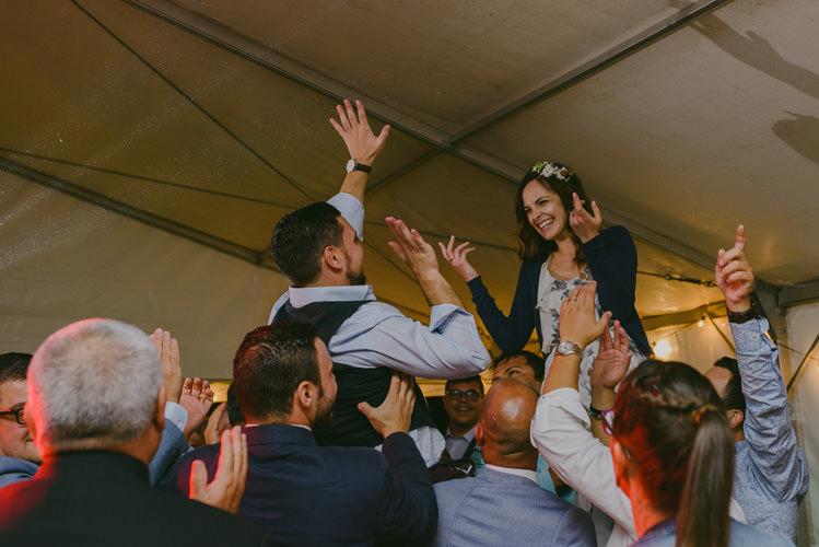 Reception Bride Patterned Floral Dress Cardigan Floral Hairpiece Groom Light Blue Shirt Dark Grey Vest Guests Dancing Natural Greenery Stylish Wedding Transylvania https://raresion.com/