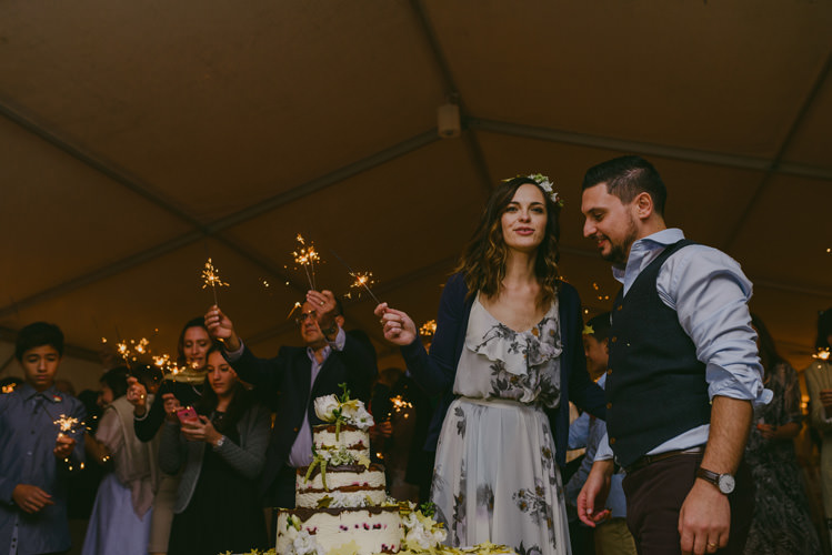 Reception Naked Wedding Cake Bride Patterned Floral Dress Cardigan Floral Hairpiece Groom Light Blue Shirt Dark Grey Vest Brown Sparklers Pants Guests Natural Greenery Stylish Wedding Transylvania https://raresion.com/
