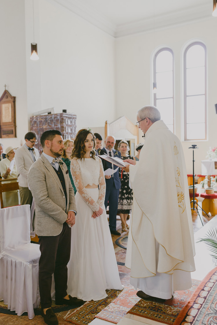 Church Ceremony Bride Two Piece Lace Bridal Gown Floral Hairpiece Groom Light Blue Shirt Sand Jacket Dark Grey Vest Brown Pants Patterned Bowtie Guests Priest Natural Greenery Stylish Wedding Transylvania https://raresion.com/