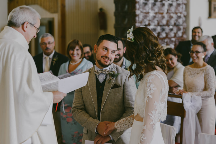 Church Ceremony Bride Two Piece Lace Bridal Gown Floral Hairpiece Groom Light Blue Shirt Sand Jacket Dark Grey Vest Brown Pants Patterned Bowtie Priest Guests Natural Greenery Stylish Wedding Transylvania https://raresion.com/