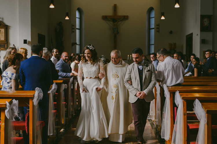 Church Ceremony Bride Two Piece Lace Bridal Gown Floral Hairpiece Groom Light Blue Shirt Sand Jacket Dark Grey Vest Brown Pants Patterned Bowtie Priest Guests Natural Greenery Stylish Wedding Transylvania https://raresion.com/