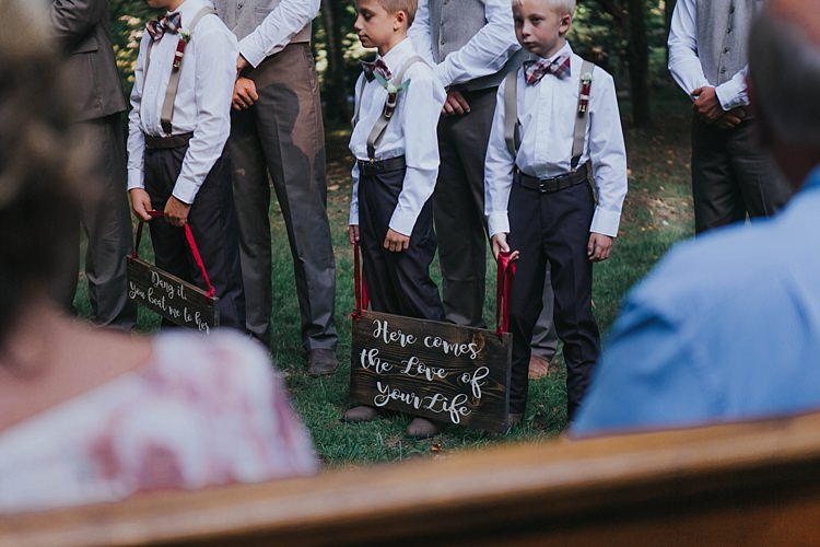 Outdoor Ceremony Page Boys Charcoal Pants White Shirts Checked Bowties Suspenders Wooden Signs Red Ribbons Bohemian & Whimsical Garden Wedding in North Carolina http://www.taylorparkerphotography.com/
