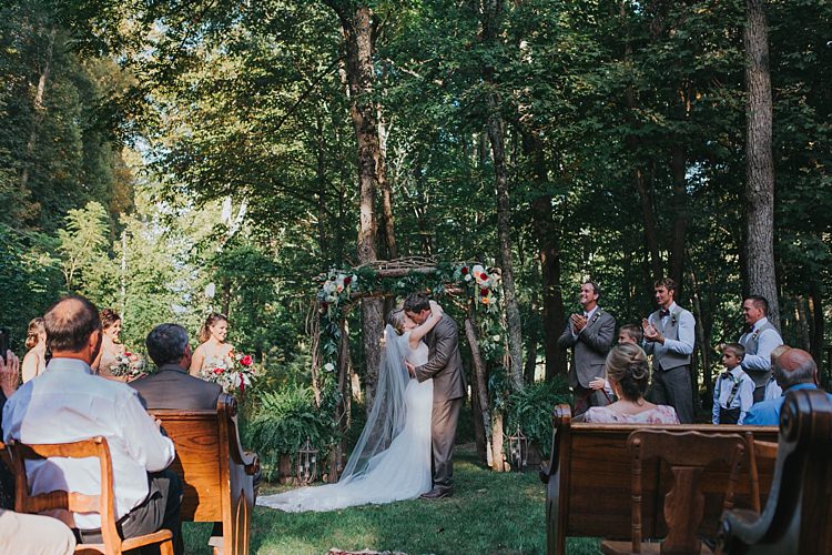 Outdoor Ceremony Floral Arch Bride Lace Embellished Gown Long Veil Groom Grey Suit Kiss Bridal Party Guests Bohemian & Whimsical Garden Wedding in North Carolina http://www.taylorparkerphotography.com/