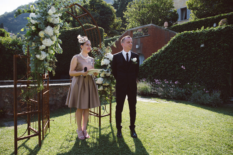 Outdoor Ceremony Groom Black Tailored Suit Black Tie Floral Buttonhole Celebrant Rusted Arch White Cream Florals Greenery Botanical Copper Greenery Lake Como Wedding http://margheritacalatiphotography.com/