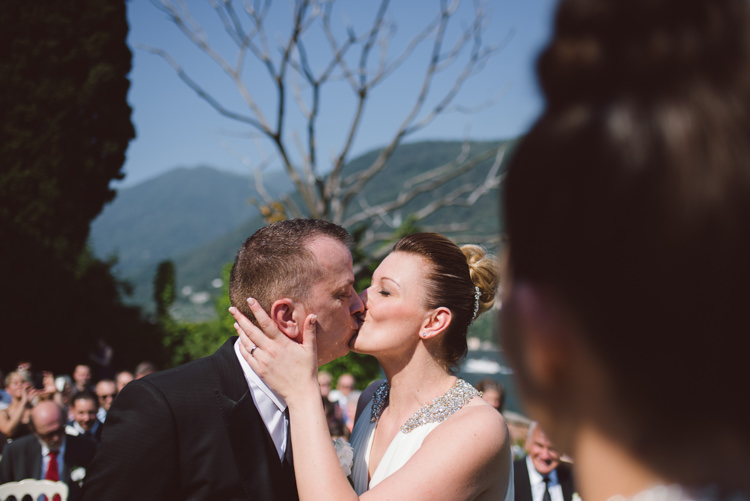 Outdoor Ceremony Bride V Neck Jenny Packham Embellished Bridal Gown Groom Tailored Black Suit White Shirt Black Tie Floral Buttonhole Kiss Guests Botanical Copper Greenery Lake Como Wedding http://margheritacalatiphotography.com/