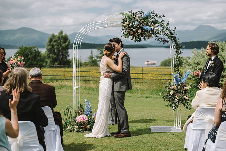 Ceremony Kiss Jenny Packham Bride Bridal Steven Purvis Bespoke Groom Prince of Wales Check Archway Pink Blue Stocks Hydrangeas Greenery Scenic Outdoor Loch Lomond Wedding http://www.lisadevinephotography.co.uk/