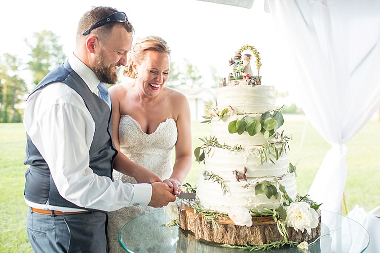Cutting Cake Rustic Figurines Topper Pets White Tiers Flowers Greenery Intimate Farmhouse Wedding South Carolina https://jessicahuntphotography.com/
