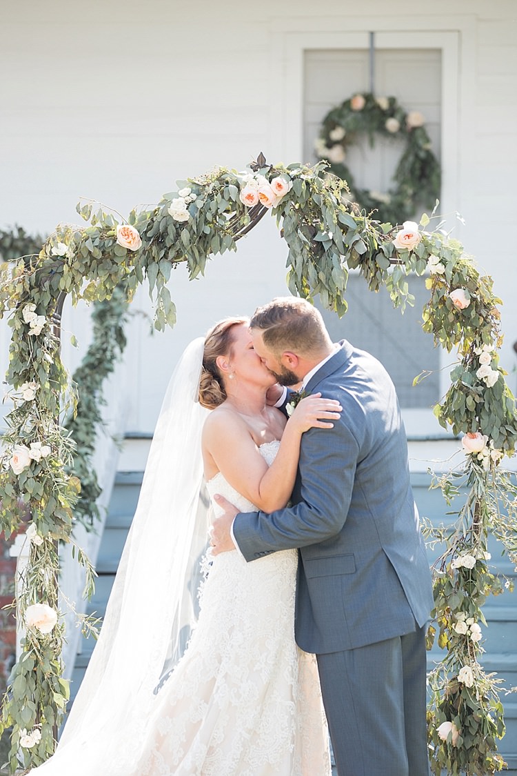 Groom Grey Suit Blue Tie Bride Long Veil Lace Dress Sweetheart Neckline Outdoor Ceremony Archway Greenery Kiss Archway Intimate Farmhouse Wedding South Carolina https://jessicahuntphotography.com/