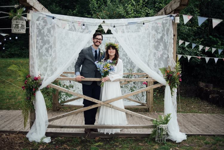 Bride Bridal Flower Crown Wildflower Bouquet Meadow long Sleeve Silk Dress 70s Grey Tweed Suit Navy Trousers Gingham Shirt Blue Lae Backdrop Bunting Lanterns Adventurous Festival Bohemian Wedding https://libertypearlphotography.com/