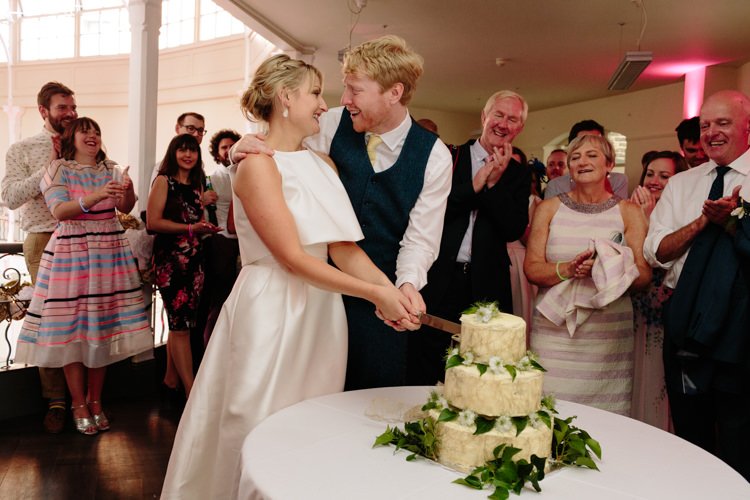 Bride Groom Cutting Cake Smiling White Green Chocolate Fudge Homemade Fresh Flowers Leaves | Modern Tropical Gold Urban Wedding https://www.christinewehrmeier.com/