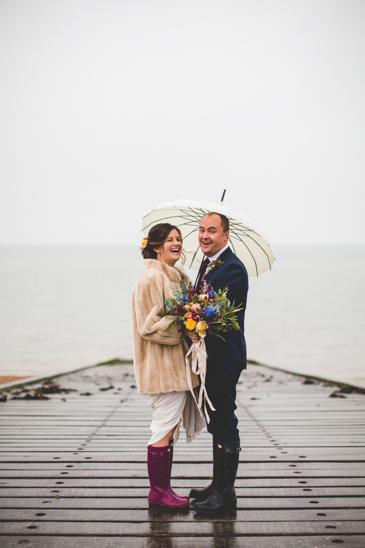 Groom Navy Suit Bride Bridal Floor Length T Shirt Neckline Short Sleeves Multicolour Wild Flower Bouquet Fur Jacket Umbrella Colourful Fun Cosy Rainy Sea Wedding http://www.livvy-hukins.co.uk/