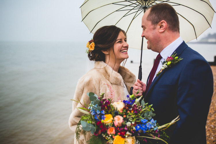 Groom Navy Suit Bride Bridal Floor Length T Shirt Neckline Short Sleeves Multicolour Wild Flower Bouquet Faux Fur Jacket Umbrella Beach Colourful Fun Cosy Rainy Sea Wedding http://www.livvy-hukins.co.uk/