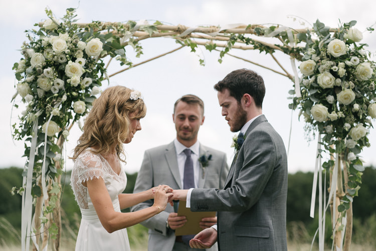 Outdoor Ceremony Arbour Arch Bride Bridal Rembo Styling Lace V Neck Dress Gown Hairpiece White Cream Rose Bouquet Eucalyptus Greenery Groom Groomsman Three Piece Grey Suit Relaxed Bohemian Summer Meadow Wedding https://karibellamy.com/