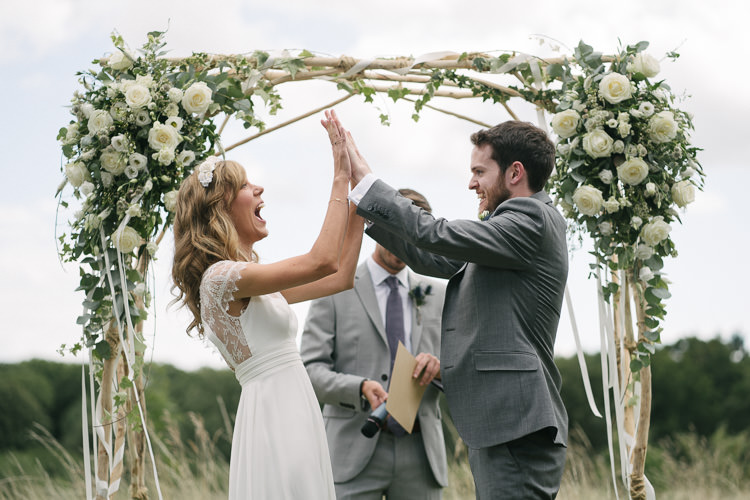 Outdoor Ceremony Arch Arbour Bride Bridal Rembo Styling Lace V Neck Dress Gown Hairpiece White Cream Rose Bouquet Eucalyptus Greenery Groom Groomsman Three Piece Grey Suit Relaxed Bohemian Summer Meadow Wedding https://karibellamy.com/