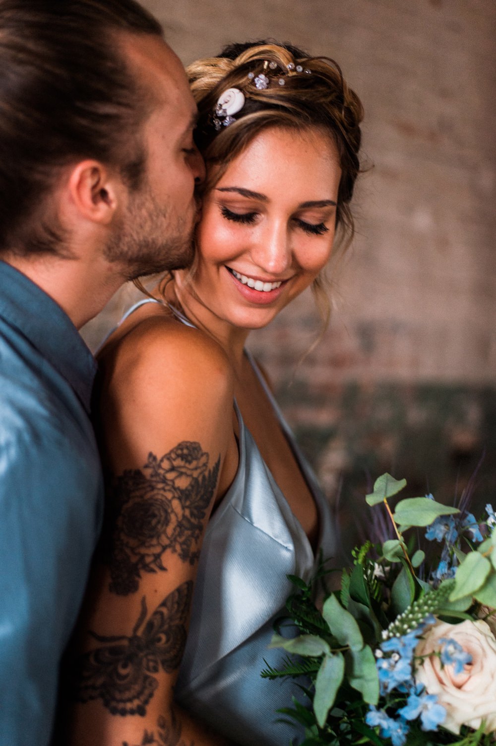 Nature Inspired Styled Shoot Seashell Headpiece Updo Tattooed Bride Blue Dress Casual Groom Blue Shirt Pastel Bouquet Kiss | Ocean Wedding Ideas Industrial Rachel Watkinson Photography