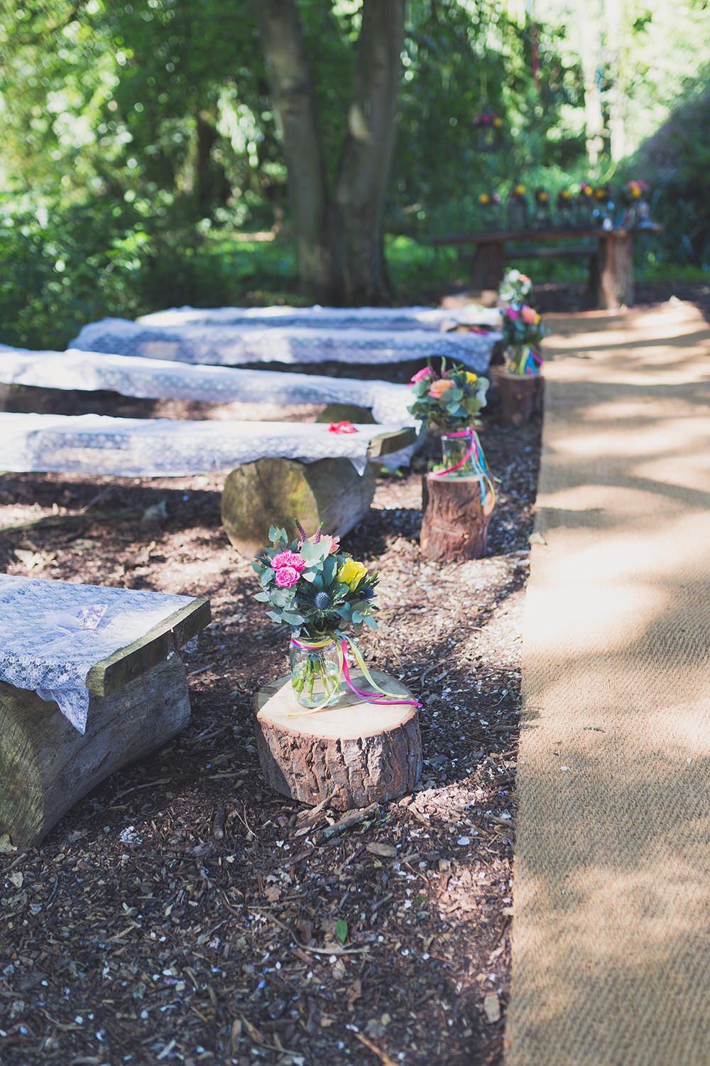 Outdoor Ceremony Wooden Benches Flowers Decor Aisle Flowers Vase Colourful Ribbons Log Stumps Hothorpe Hall Woodlands Wedding Lucy Long Photography