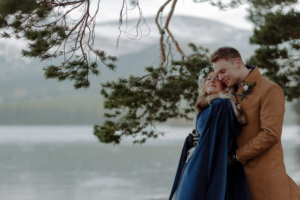 Forest Trees Castle Loch Bride Groom Blue Dress White Bouquet Floral Crown Cape Tan Coat | Intimate Winter Outdoor Scotland Wedding Christopher Ian Photography