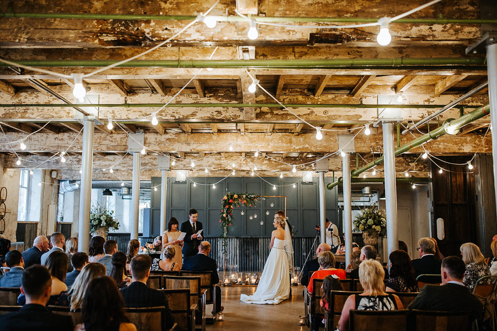 Ceremony Warehouse Industrial Festoon Lights Flowers Backdrop Arch Aisle Holmes Mill Wedding Emilie May Photography