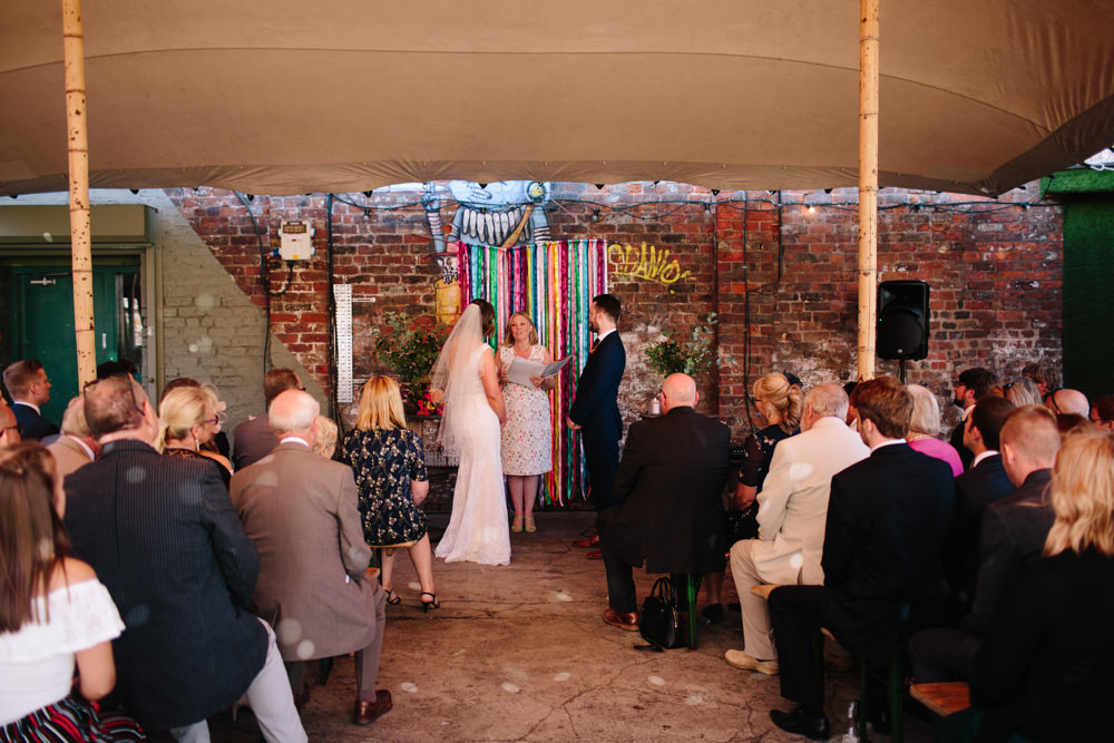 Bride Bridal Watters Lace Sleeveless Dress Gown Navy Suit Groom Colourful Multicoloured Ribbon Backdrop Veil Constellations Liverpool Wedding Dan Hough Photo