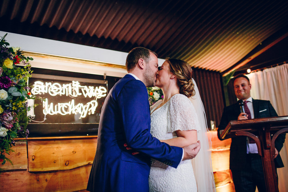 Bride Bridal V Neck Sleeves Beaded Detail Dress Gown Blue Suit Groom Neon Sign Ceremony Tatton Wedding Stock Farm Barn Amy B Photography