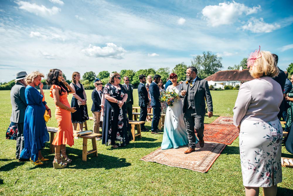 Ceremony Village Hall Essex Persian Rug Aisle Frame Arch Backdrop Greenery Foliage Flowers Benches Outdoor DIY Wedding Three Flowers Photography