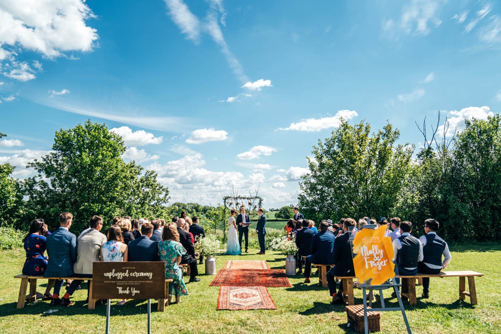 Ceremony Village Hall Essex Persian Rug Aisle Frame Arch Backdrop Greenery Foliage Flowers Benches Outdoor DIY Wedding Three Flowers Photography
