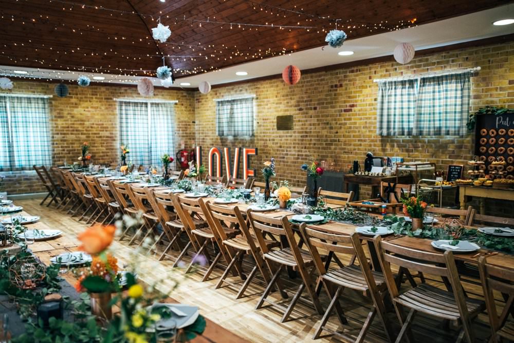 Long Rustic Wooden Tables Folding Chairs Pom Poms Village Hall Fairy Lights Outdoor DIY Wedding Three Flowers Photography