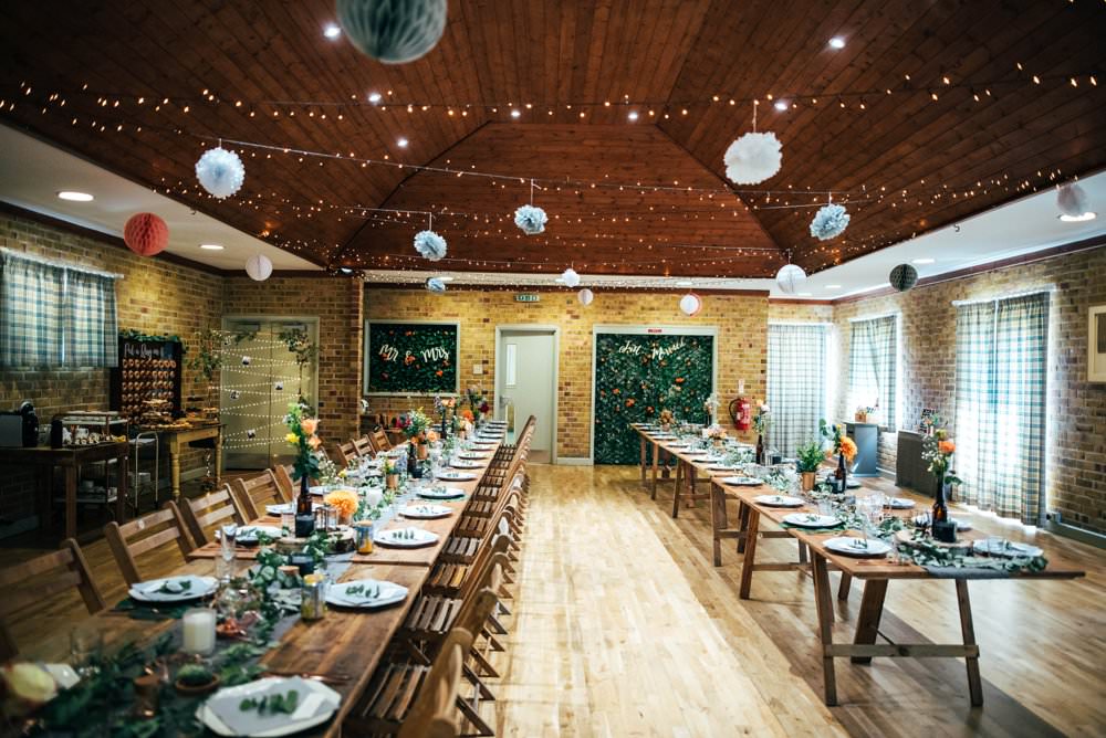 Long Rustic Wooden Tables Folding Chairs Pom Poms Village Hall Fairy Lights Outdoor DIY Wedding Three Flowers Photography