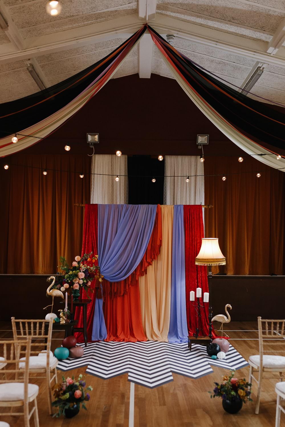 Ceremony Backdrop Drapes Fabric Monochrome Rug Festoon Lights Flowers Village Hall Wedding Emily + Katy Photography