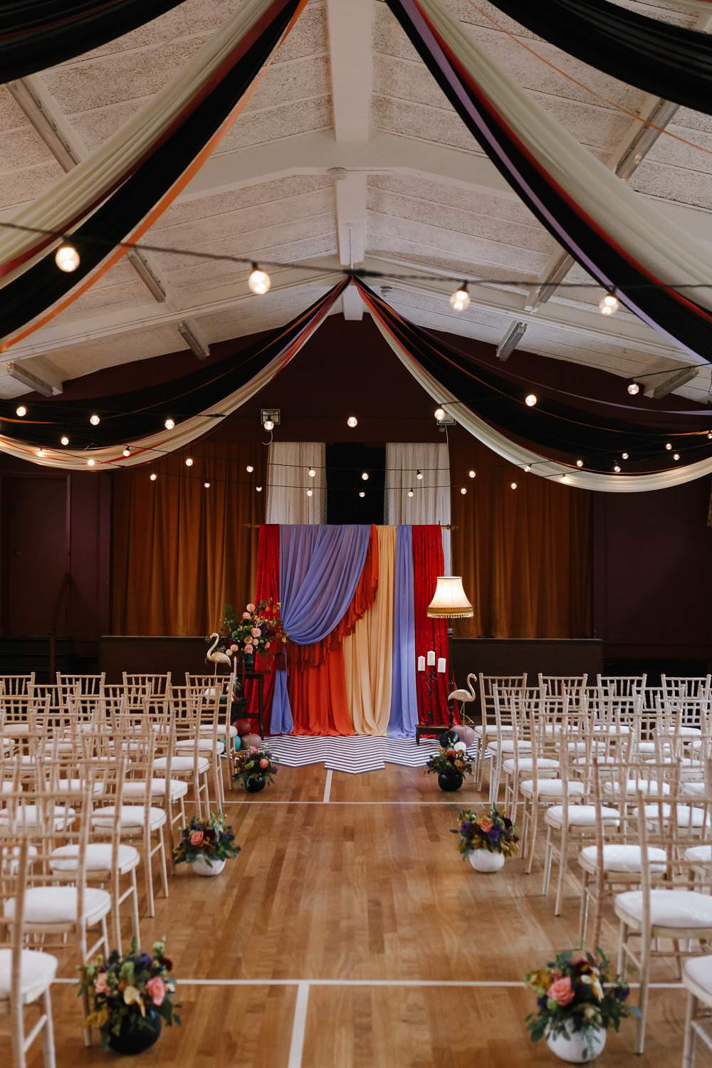 Ceremony Backdrop Drapes Fabric Monochrome Rug Festoon Lights Flowers Village Hall Wedding Emily + Katy Photography