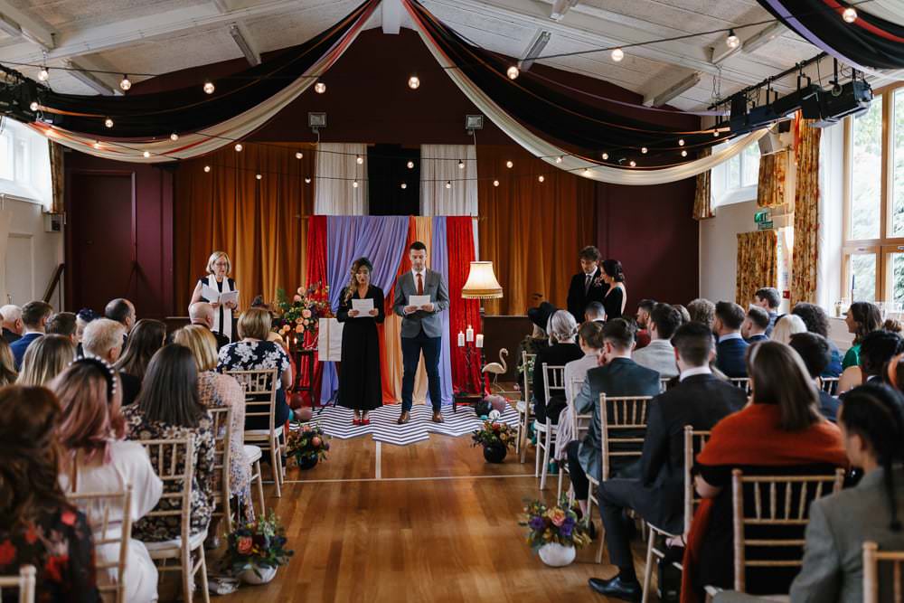 Ceremony Backdrop Drapes Fabric Monochrome Rug Festoon Lights Flowers Village Hall Wedding Emily + Katy Photography