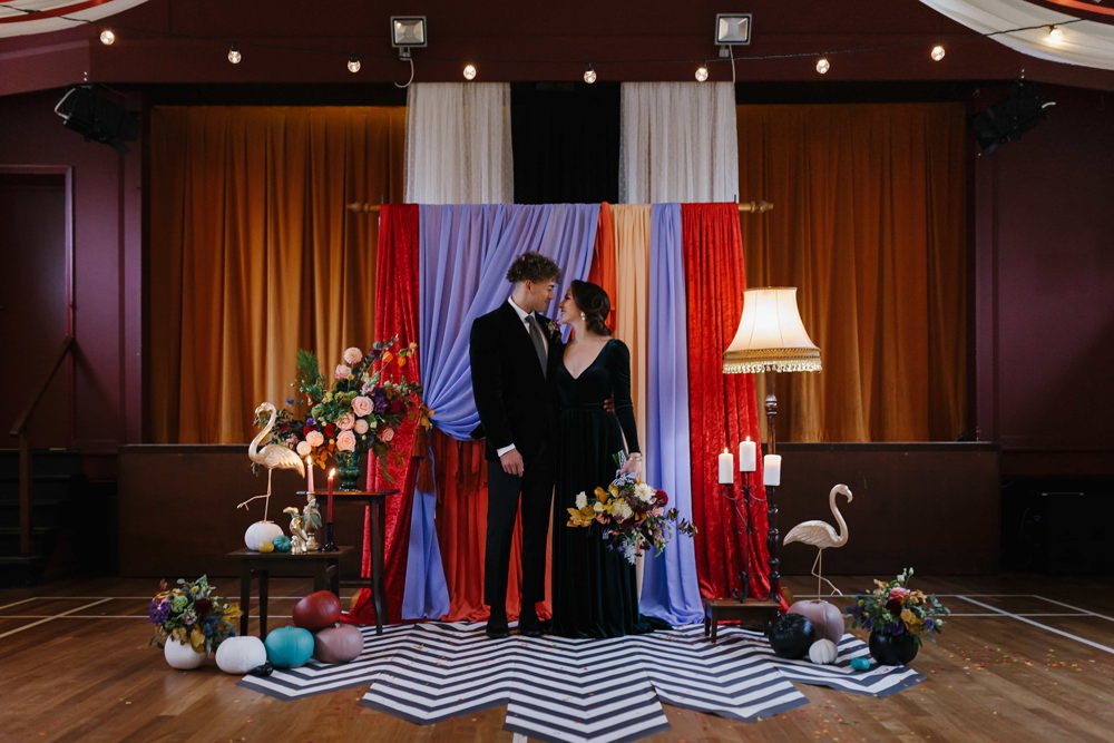 Village Hall Wedding Emily + Katy Photography Ceremony Backdrop Drapes Fabric Monochrome Rug Festoon Lights Flowers