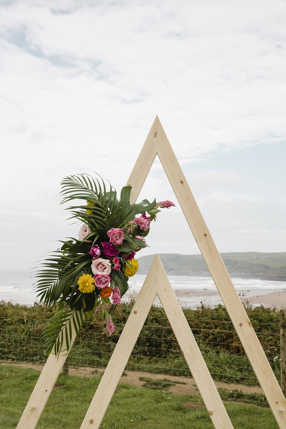 Outdoor Ceremony Beach Sea Triangle Arch Backdrop Flowers Tiki Wedding AW Wedding Photography