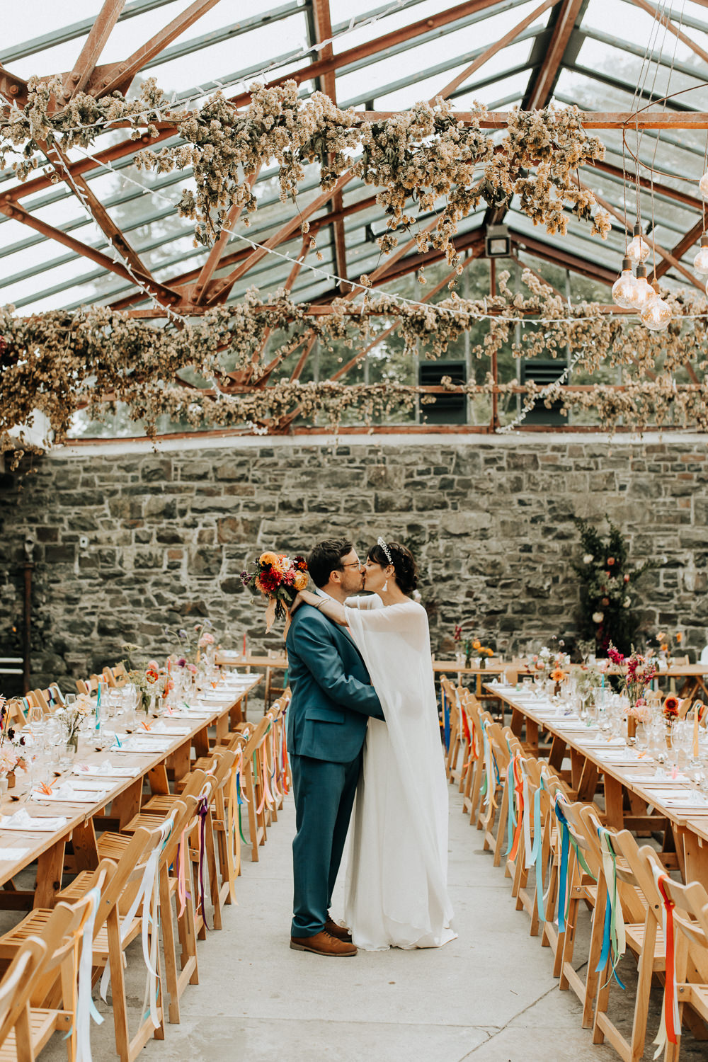 Glass House Conservatory Reception Wooden Chairs Rainbow Ribbons Long Tables Flowers Decor Plas Dinam Wedding Wyldbee Photography