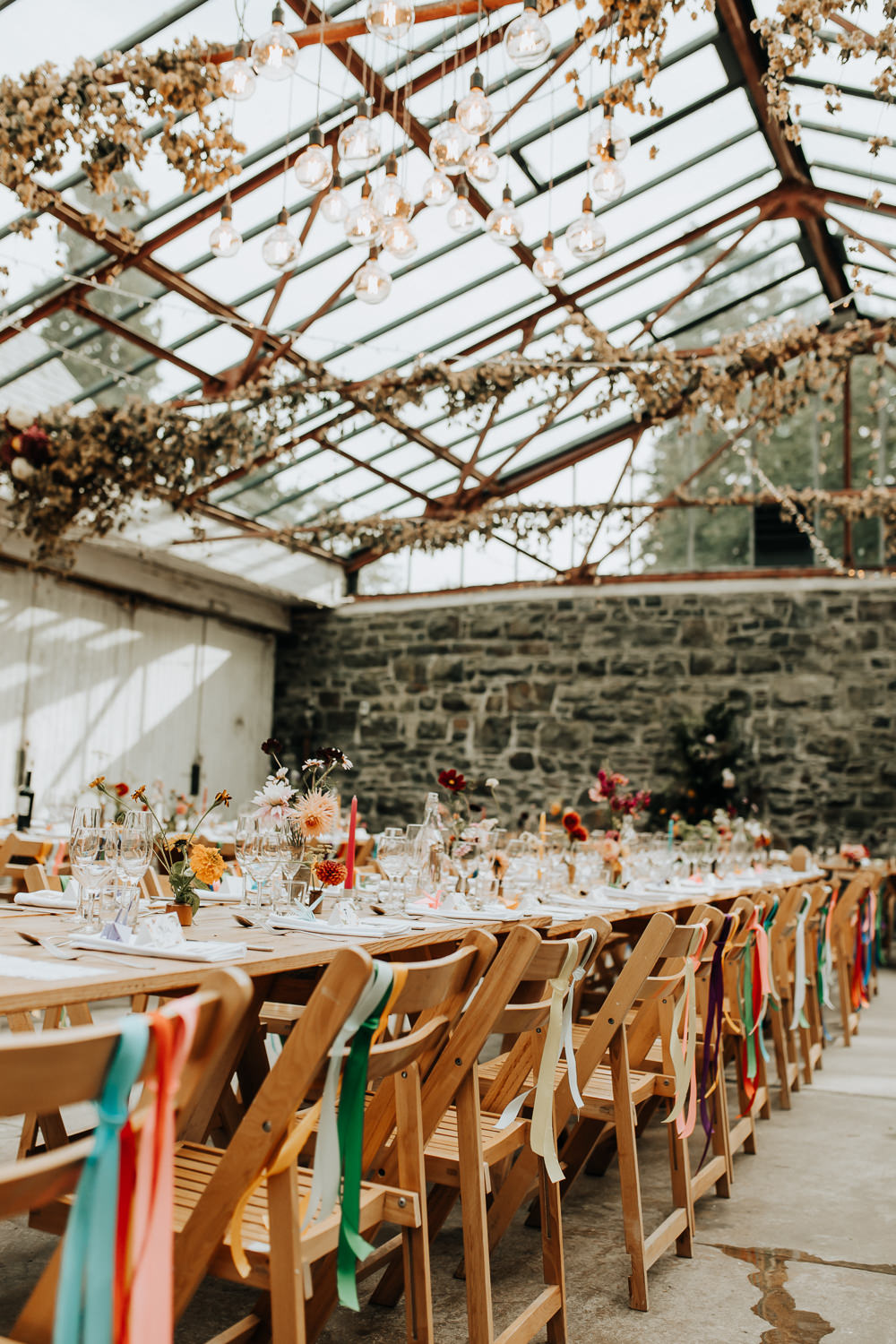 Glass House Conservatory Reception Wooden Chairs Rainbow Ribbons Long Tables Flowers Decor Plas Dinam Wedding Wyldbee Photography