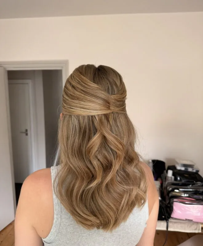 A back view of a bride showing a half up half down hairstyle with soft, flowing waves during morning preparations.